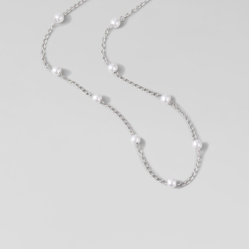 Nura Pearl Silver Necklace, laid flat on a light grey surface, pearls spaced along silver chain