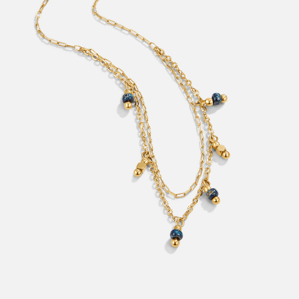 Olivia Blue Droplet Necklace, flat lay of a layered gold necklace with blue bead drops