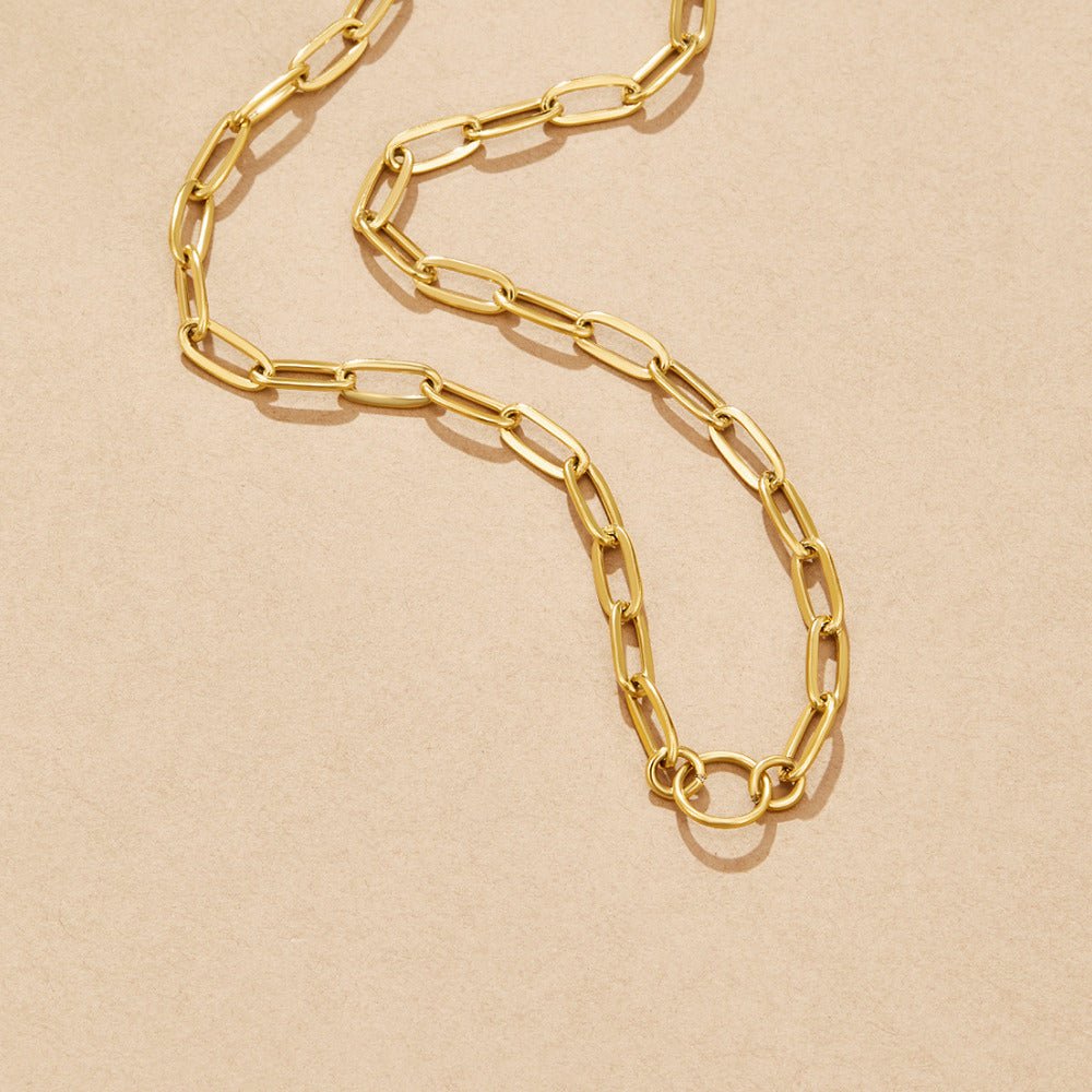 Pia Chain Link Charm Necklace, laid flat on a beige surface, curving into an S shape