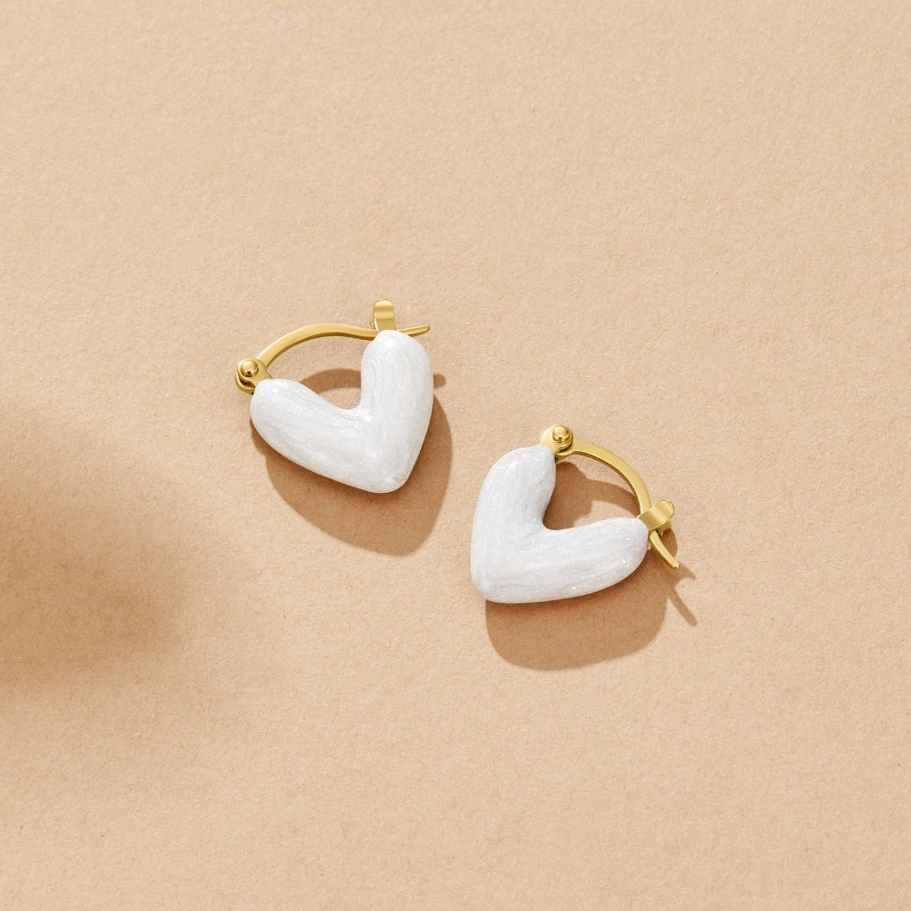 ‘Pure Love’ Heart Earrings, pair of white enamel heart hoops on a beige surface