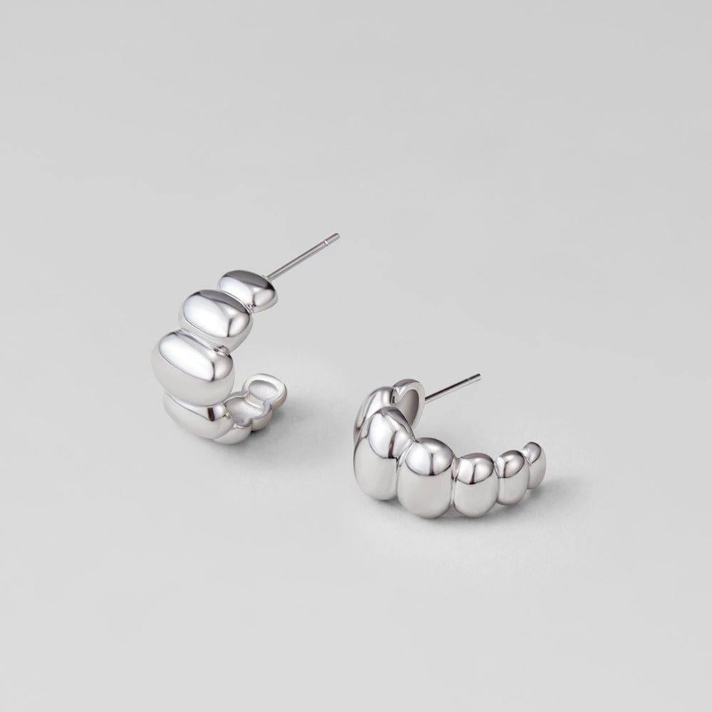 Rene Silver Puff Earrings, pair of polished silver puffed hoop earrings on a grey surface