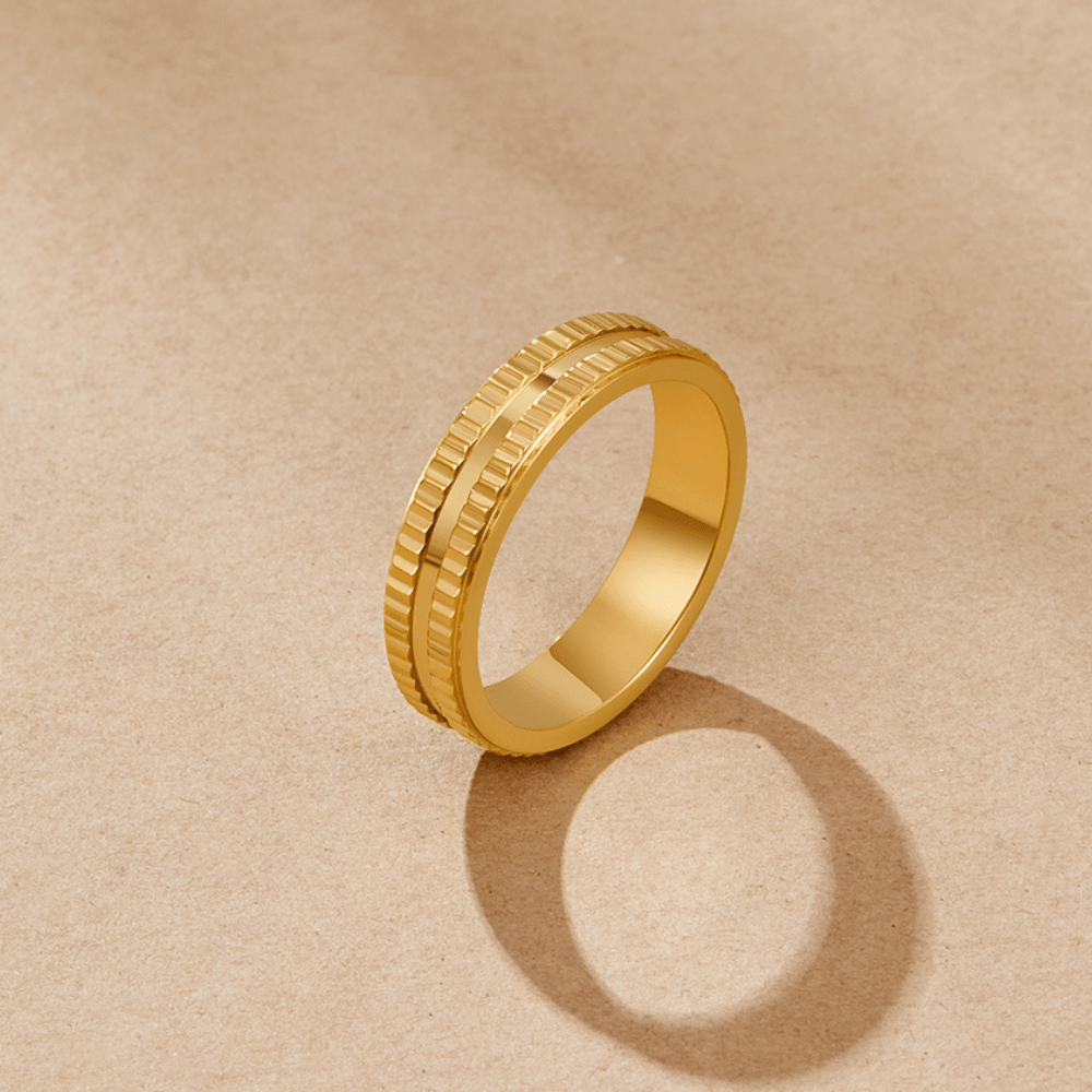 Rina Gold Band Ring, standing upright on a beige paper backdrop, casting a shadow