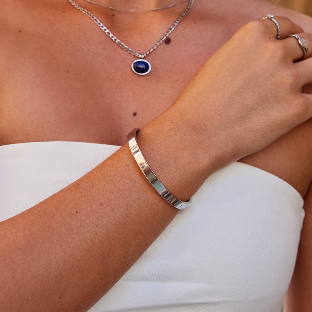 Rina Silver Bangle, worn on a wrist with a navy pendant necklace and rings