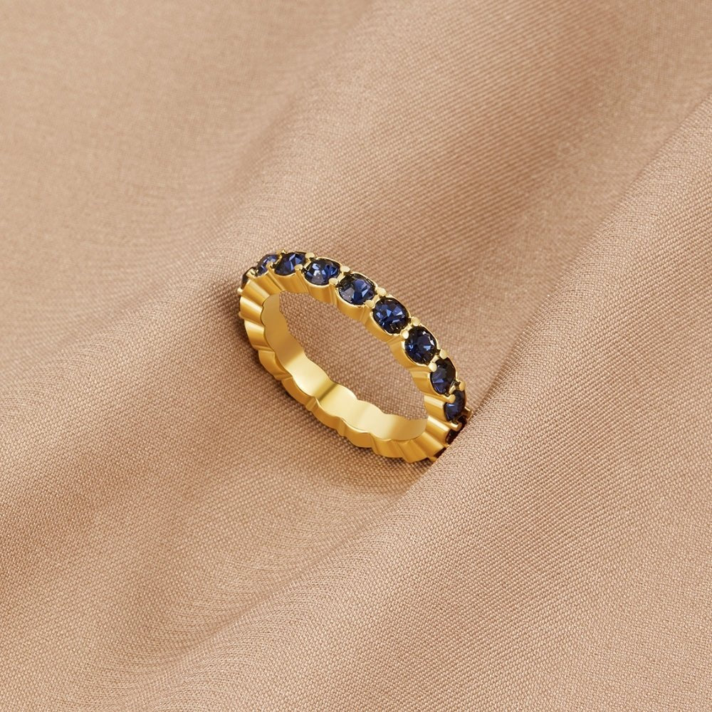 Sapphire Beauty 18k Crystal Ring, gold band with a row of blue stones, lying on beige fabric