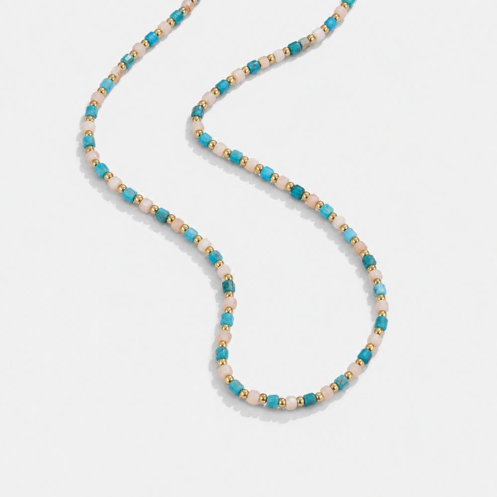Alashan Blue Bead Necklace, laid flat on a pale grey surface, curving in an S-shape, blue and