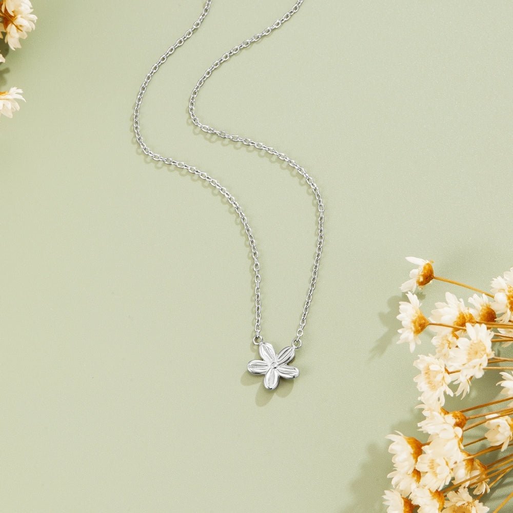 Silver Blossom Pendant Necklace, laid flat on sage green with dried white flowers beside it