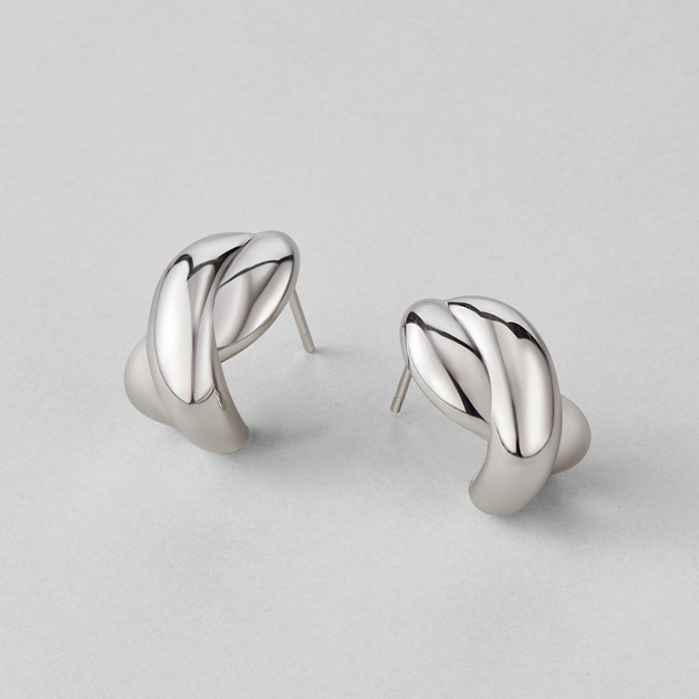 Silver Dakota Twisted Earrings, pair of polished silver twisted earrings lying on a grey surface
