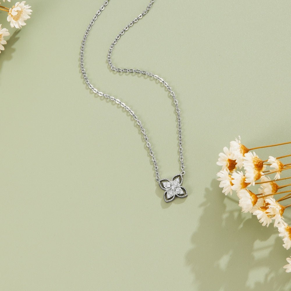 Silver Four Leaf Crystal Necklace, flat lay on sage green, with dried white flowers beside it
