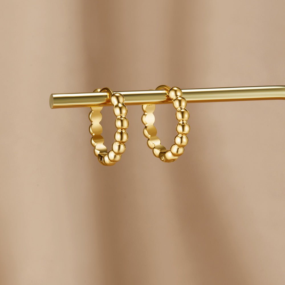 Soraya Gold Bead Hoop Earrings, hanging on a gold bar against a beige backdrop