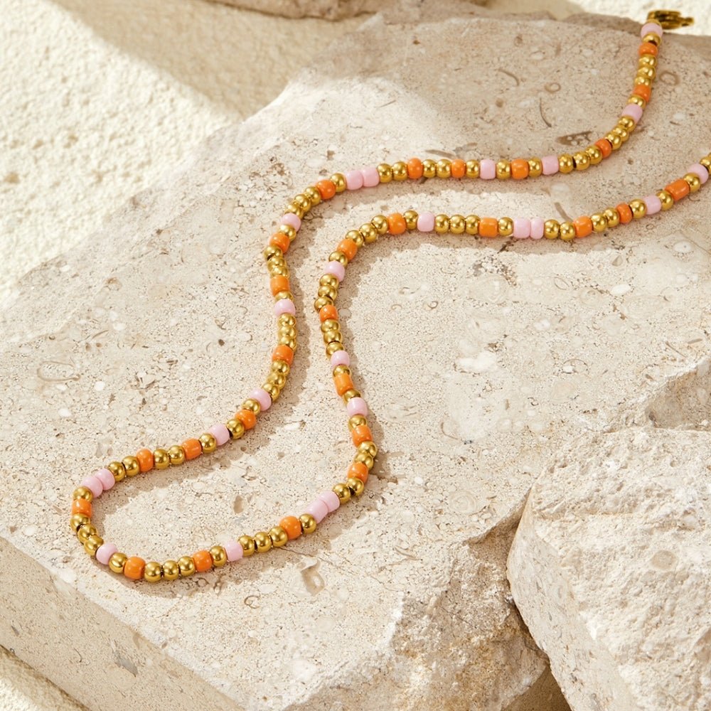 Sunset Glow Bead Necklace, laid across pale stone with orange, pink and gold beads