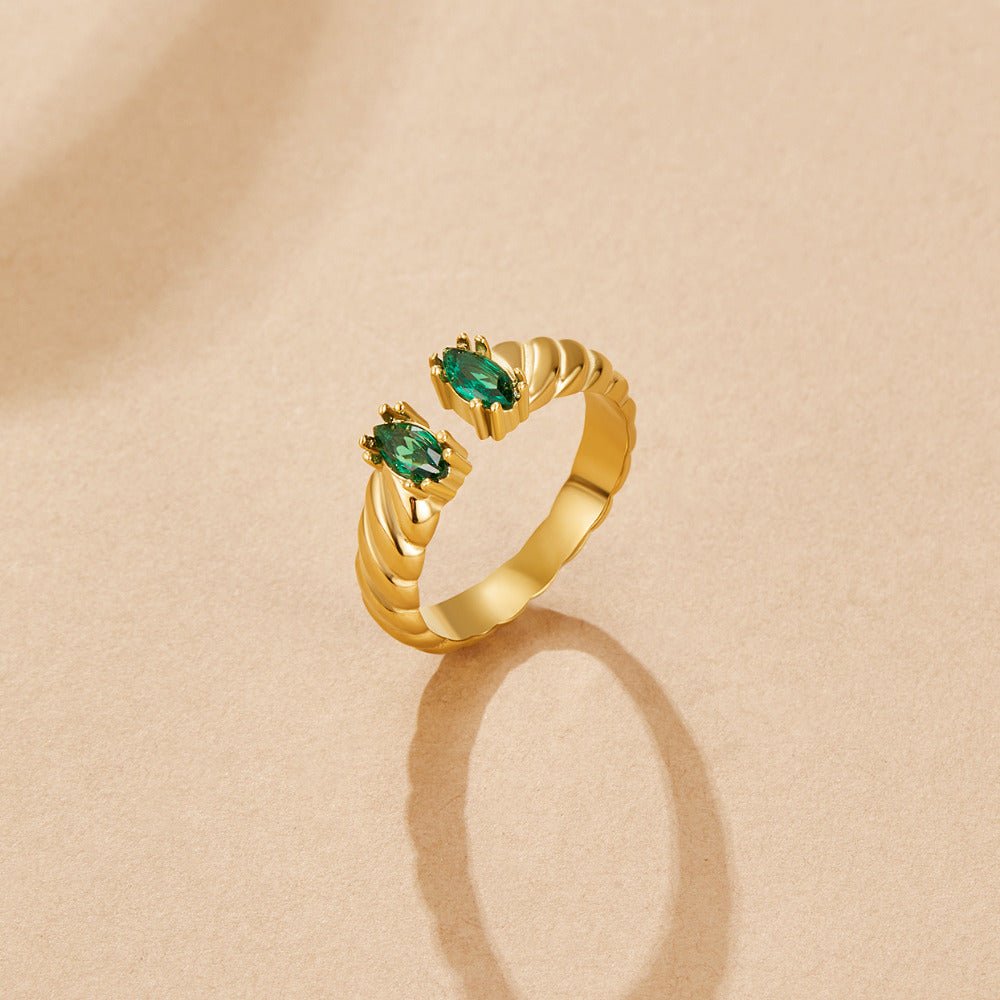 Tara Vintage Emerald Ring, open gold ring with two oval green stones on a beige surface