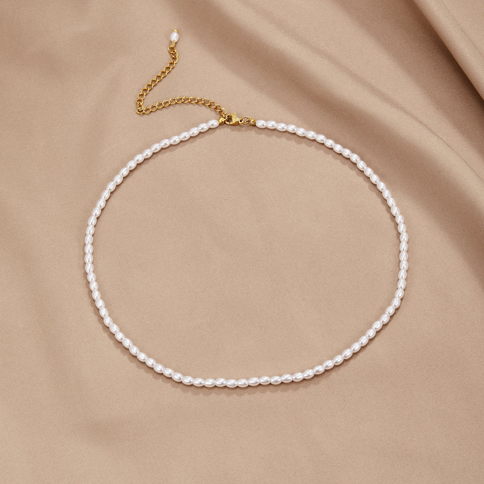 Temi Pearl Necklace, laid flat on beige satin, gold clasp and extender chain visible