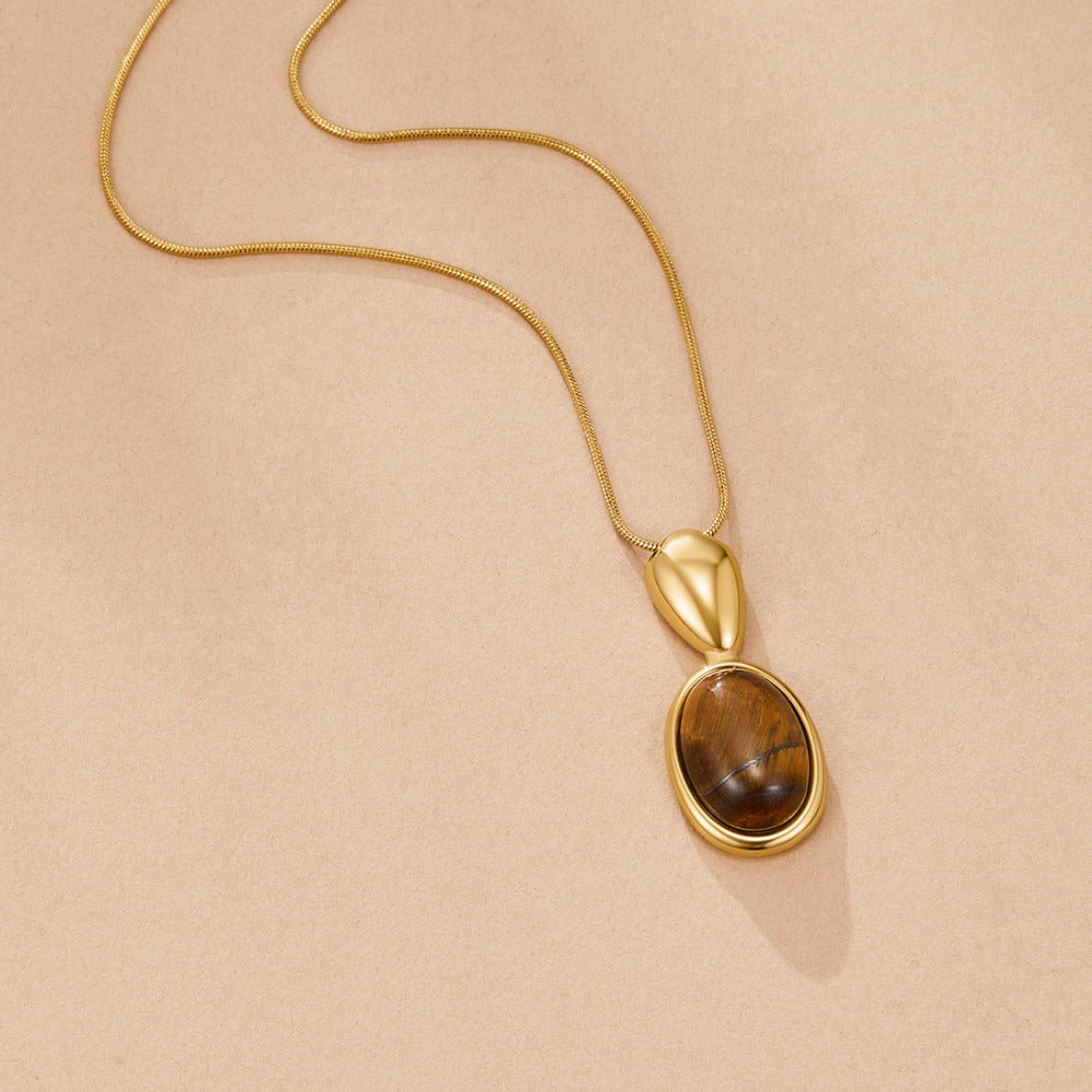 Tiger Eye Stone Long Necklace, laid flat on beige fabric, gold chain with brown oval stone pendant