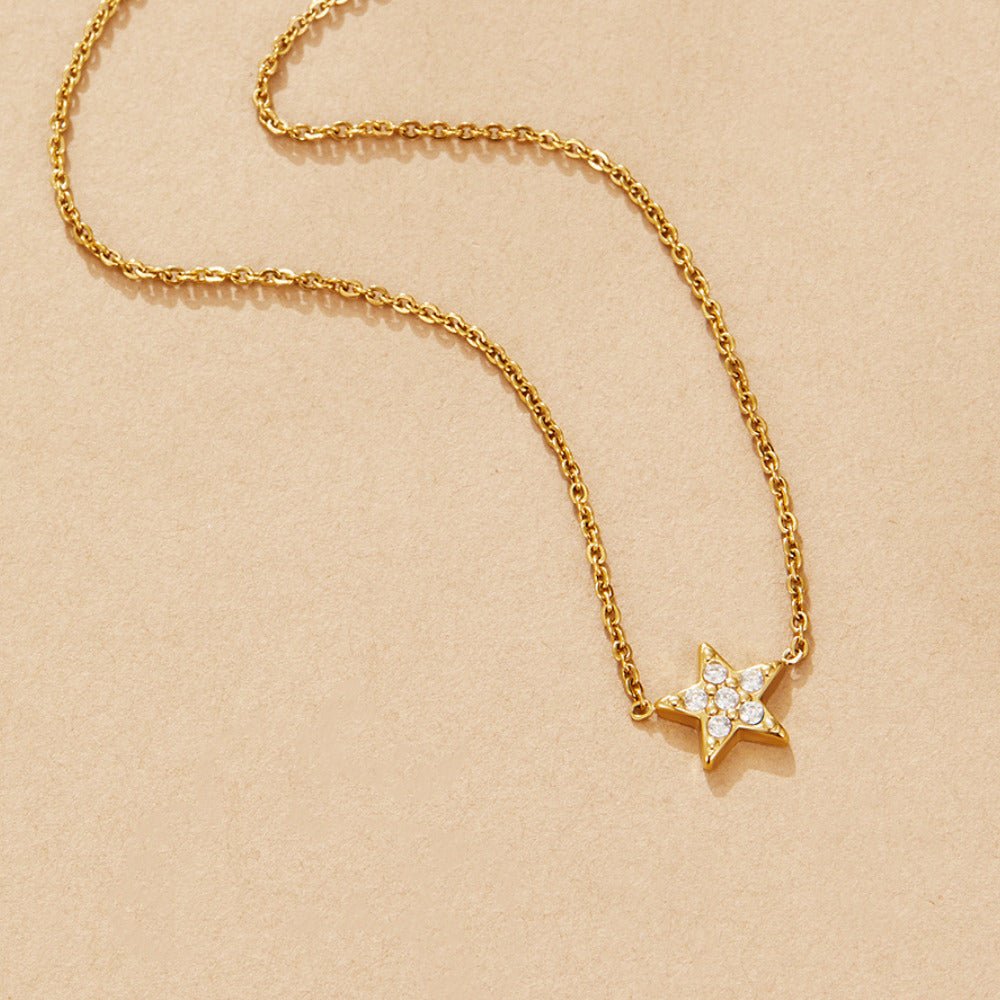 Tiny 'Shooting Star' Necklace, laid flat on a beige surface, gold chain with pavé star pendant