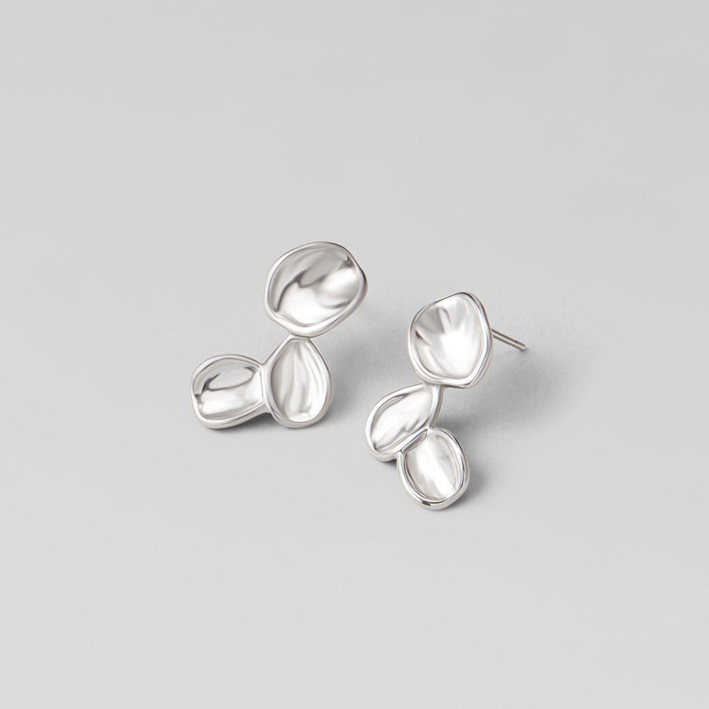 Tori Silver Petal Drop Earrings, a pair of silver earrings lying flat on a light grey surface