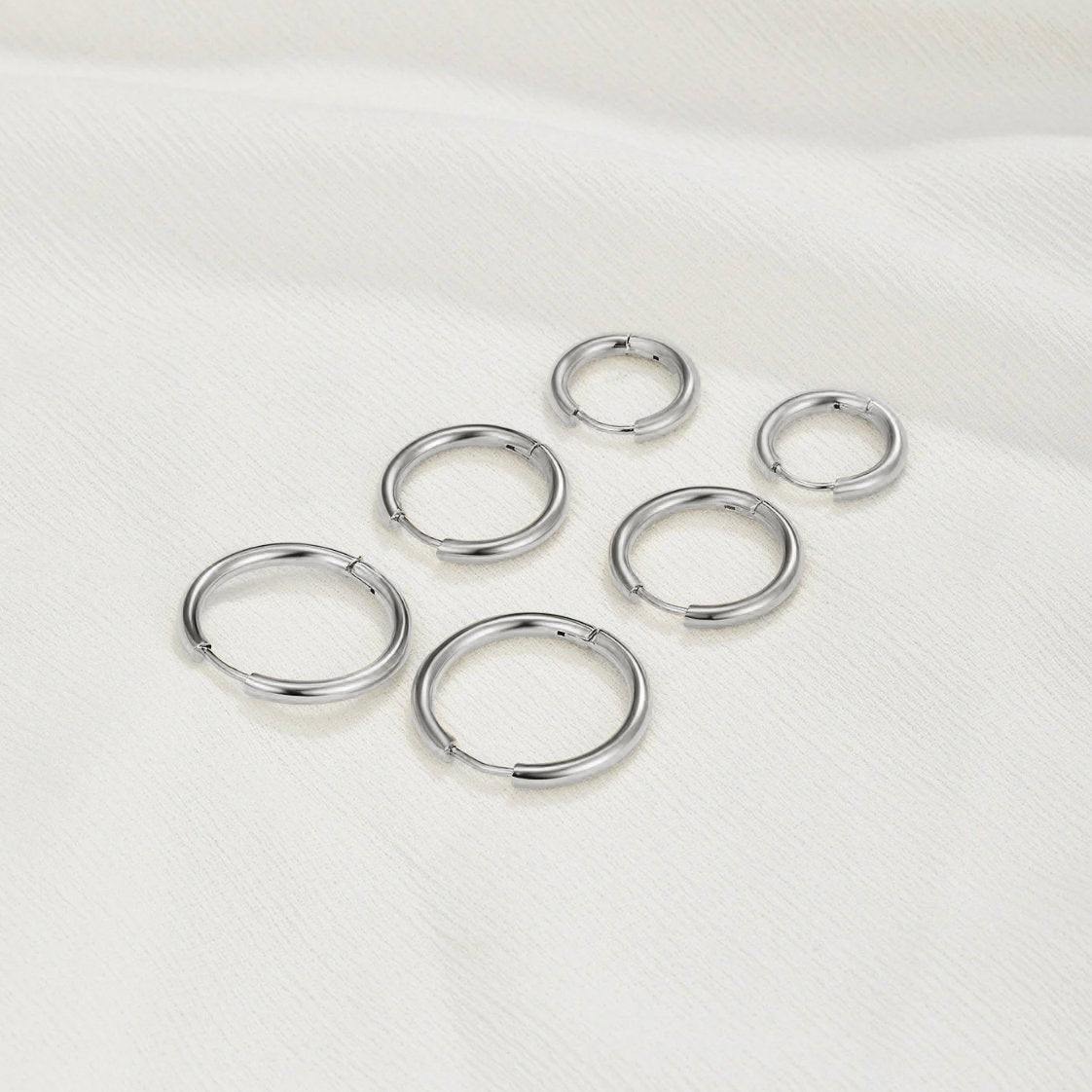 Triple Hoop Earrings Silver Set, six silver hoop earrings in three sizes laid on white fabric