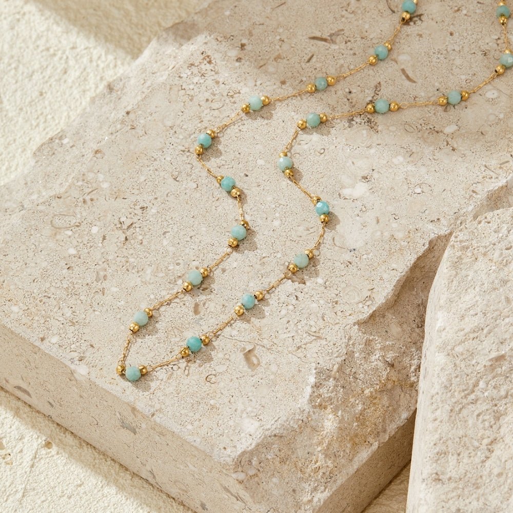 Turquoise Bead Chain Necklace, laid across a pale stone block, gold chain with turquoise beads
