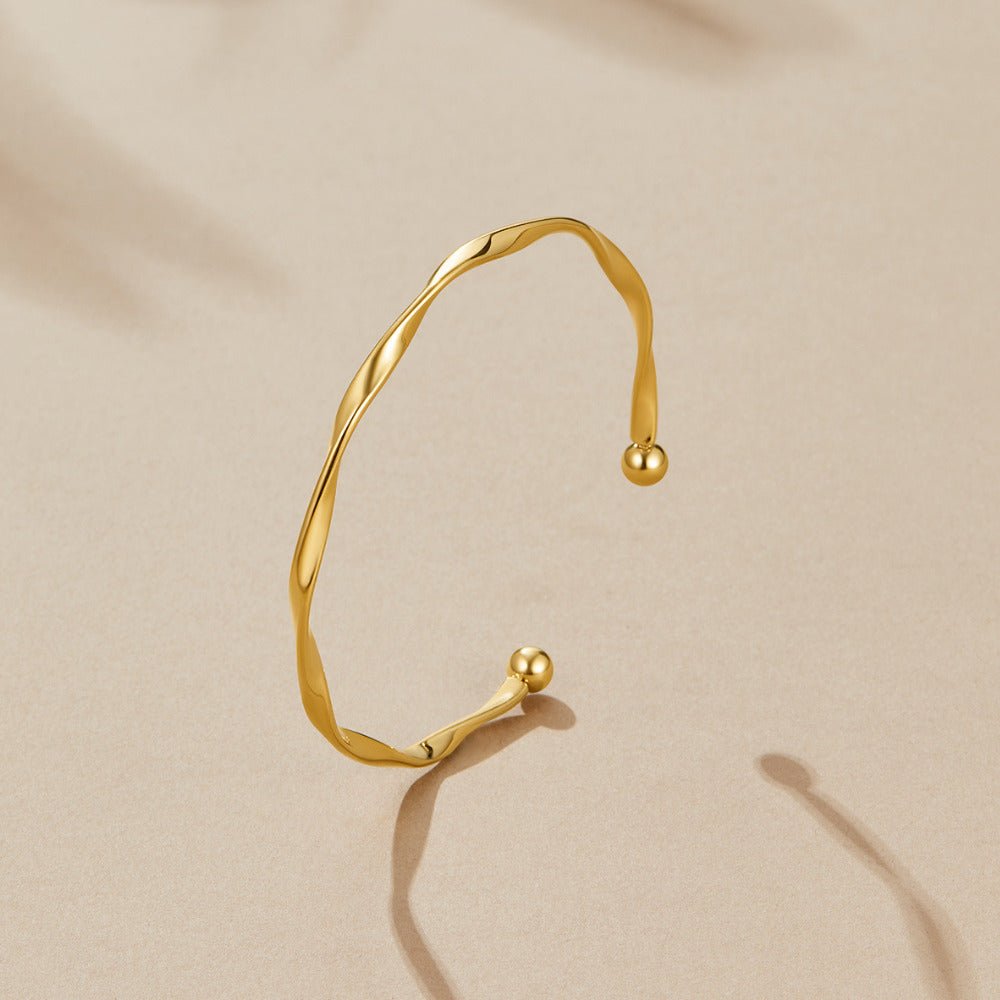 Twisted Imari Gold Bangle, open gold cuff bangle lying flat on a beige surface, ball ends