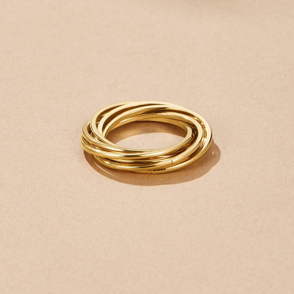Twisted Mia Gold Ring, interlocking gold bands lying on a beige surface, viewed from above