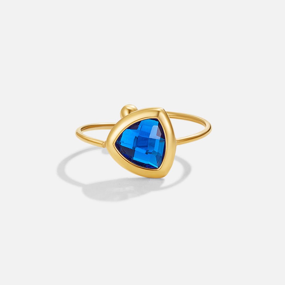 Via Sapphire Blue Ring, gold ring with a faceted blue triangular stone on white background