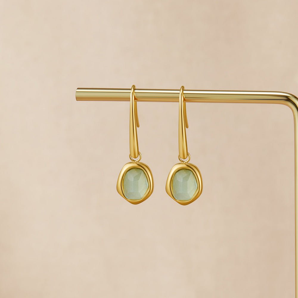 Vintage Aquamarine Drop Earrings, hanging on a gold bar against a beige backdrop, pale green stones