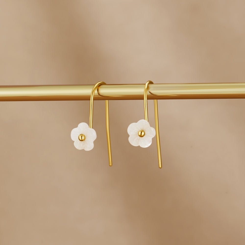 White Petal Shell Drop Earrings, hanging on a gold rod against a beige backdrop