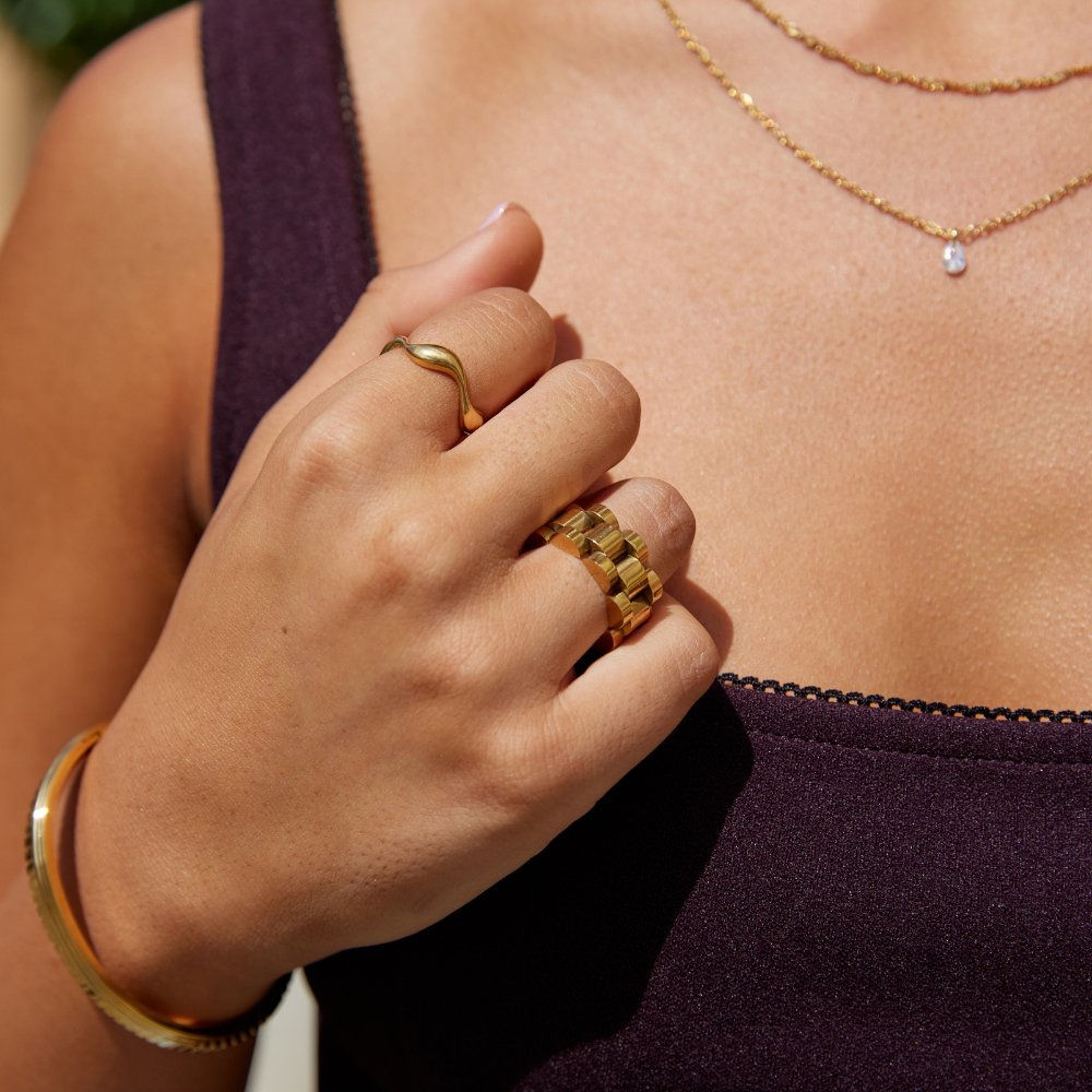 18K Gold Wave Ring, worn on a hand with a chunky link ring and gold bangle