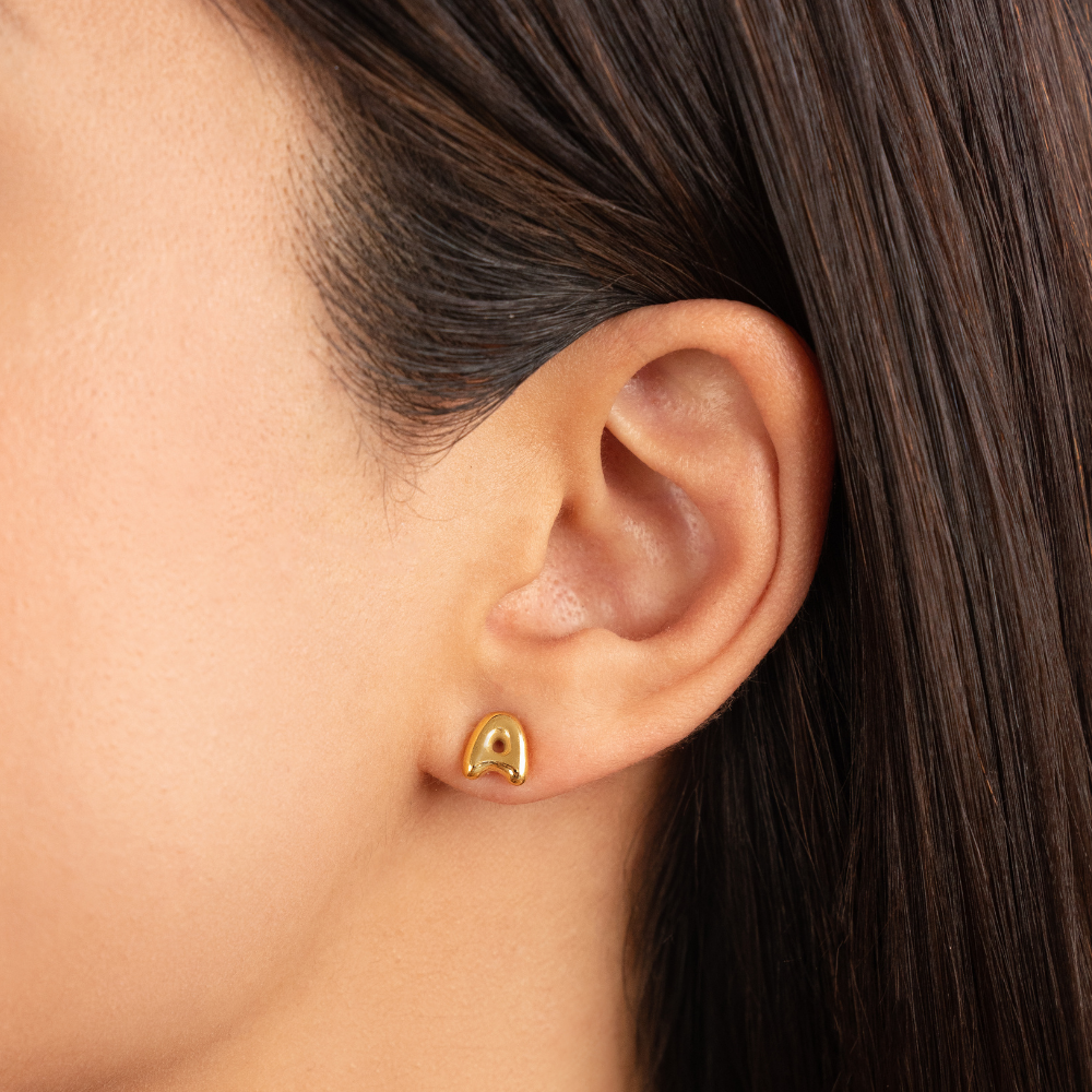 Gold Bubble Letter Earrings, worn on an ear, close-up of a glossy gold stud