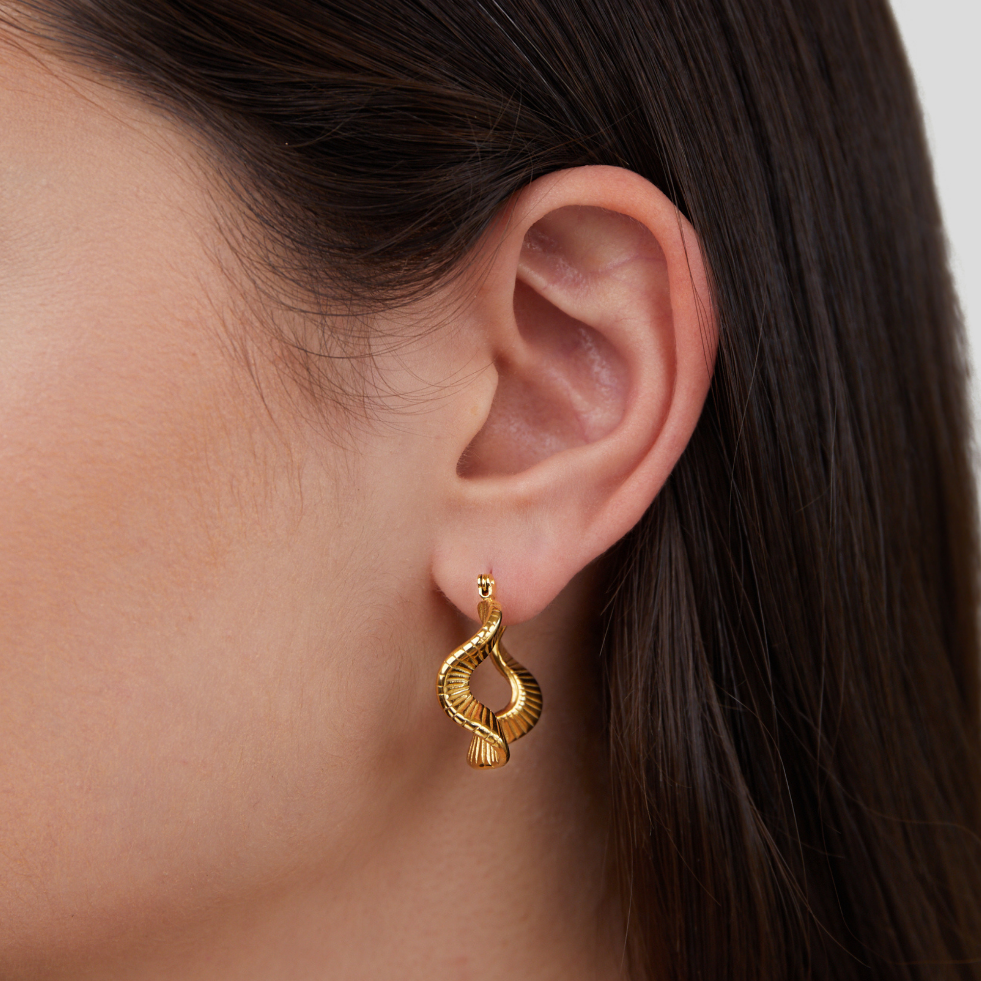 Geometric Wave Gold Hoop Earrings, worn on an ear, close-up with gold ribbed twisted drop