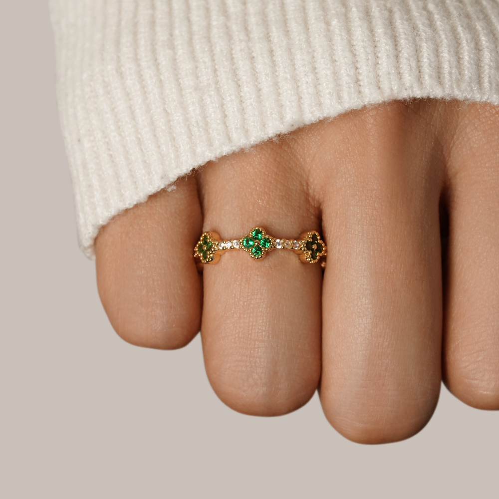 Four Leaf Clover Crystal Ring, worn on a finger with a cream knit sleeve, green clover motifs