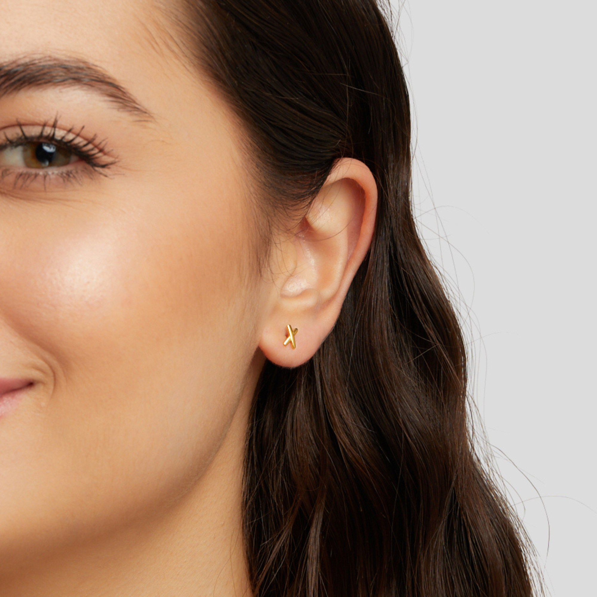 Graffiti X Stud Earrings, worn in an ear, small gold X-shaped stud