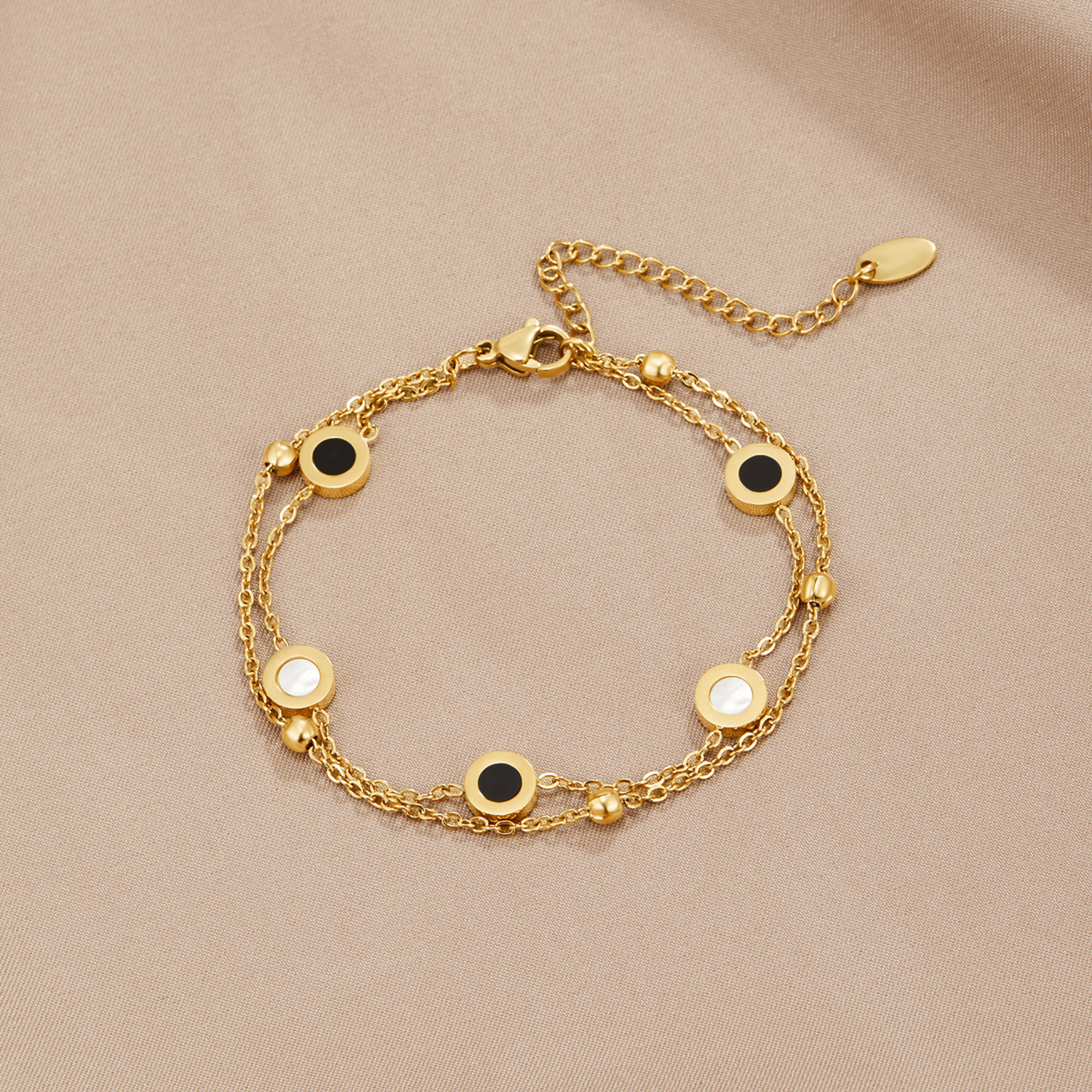 Onyx & White Stone Bracelet, laid flat on beige fabric, gold double chain with black and white
