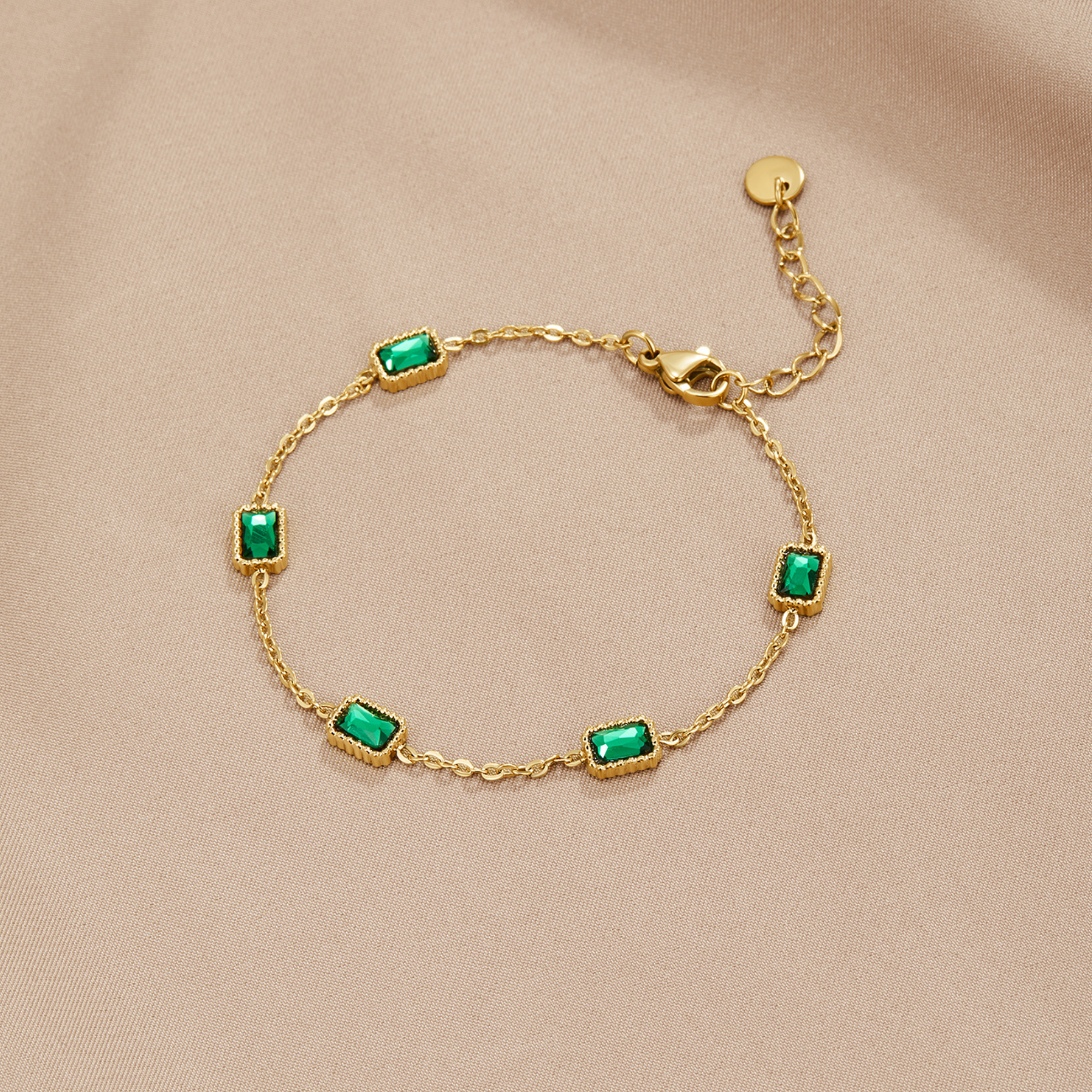 Trinity Emerald Bracelet, laid flat on beige satin, five green emerald-cut stones in gold settings