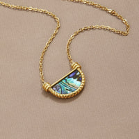 Amalfi Turquoise Shell Necklace, laid flat on a taupe fabric, gold chain with half-moon shell