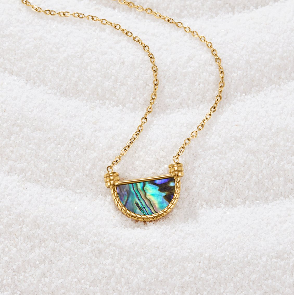 Amalfi Turquoise Shell Necklace, laid on white sand, gold chain with iridescent shell pendant