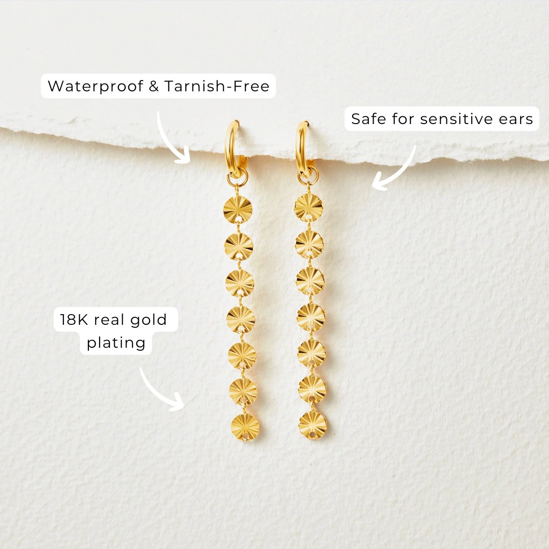 Amari 18K Gold Disc Earrings, a pair of gold drop earrings hanging against white paper