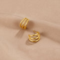 Anaya Triple Gold Hoop Earrings, two gold triple-band hoop earrings lying on beige fabric