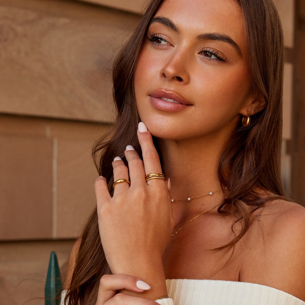 Ara Twisted Crossed Ring, worn on a hand with gold rings and a pearl necklace