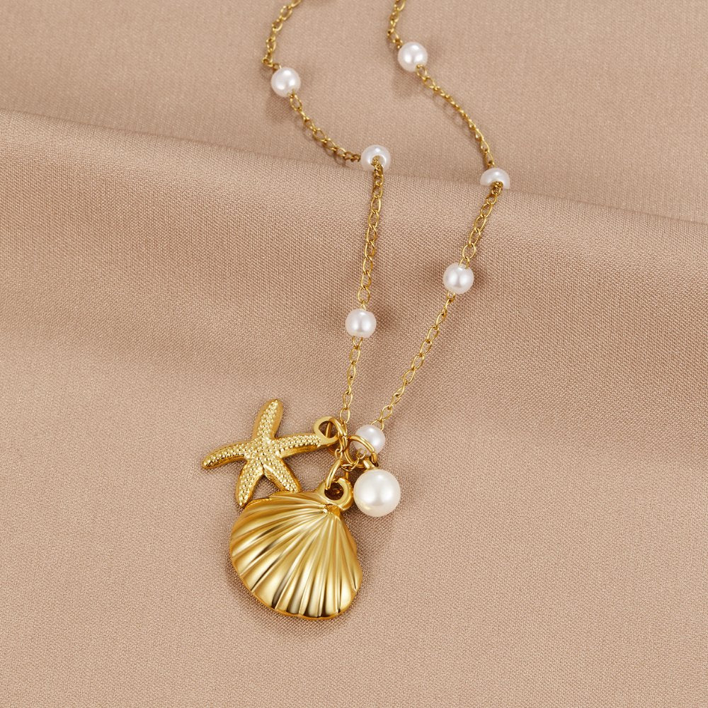 Aria Shell Charm Necklace, laid flat on beige satin with gold shell, starfish and pearl charms
