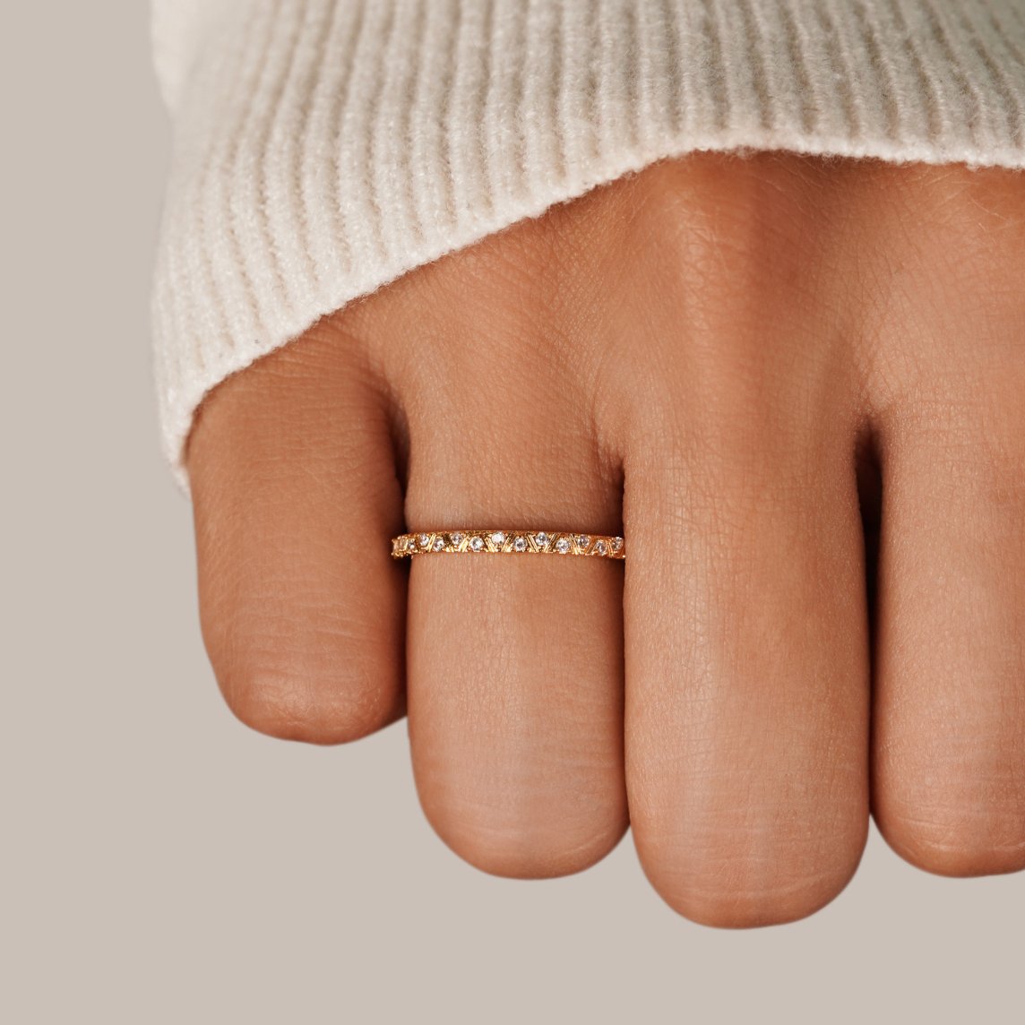 Arquette Gold & Crystal Band Ring, worn on a hand in a cream knit sleeve, gold band with stones