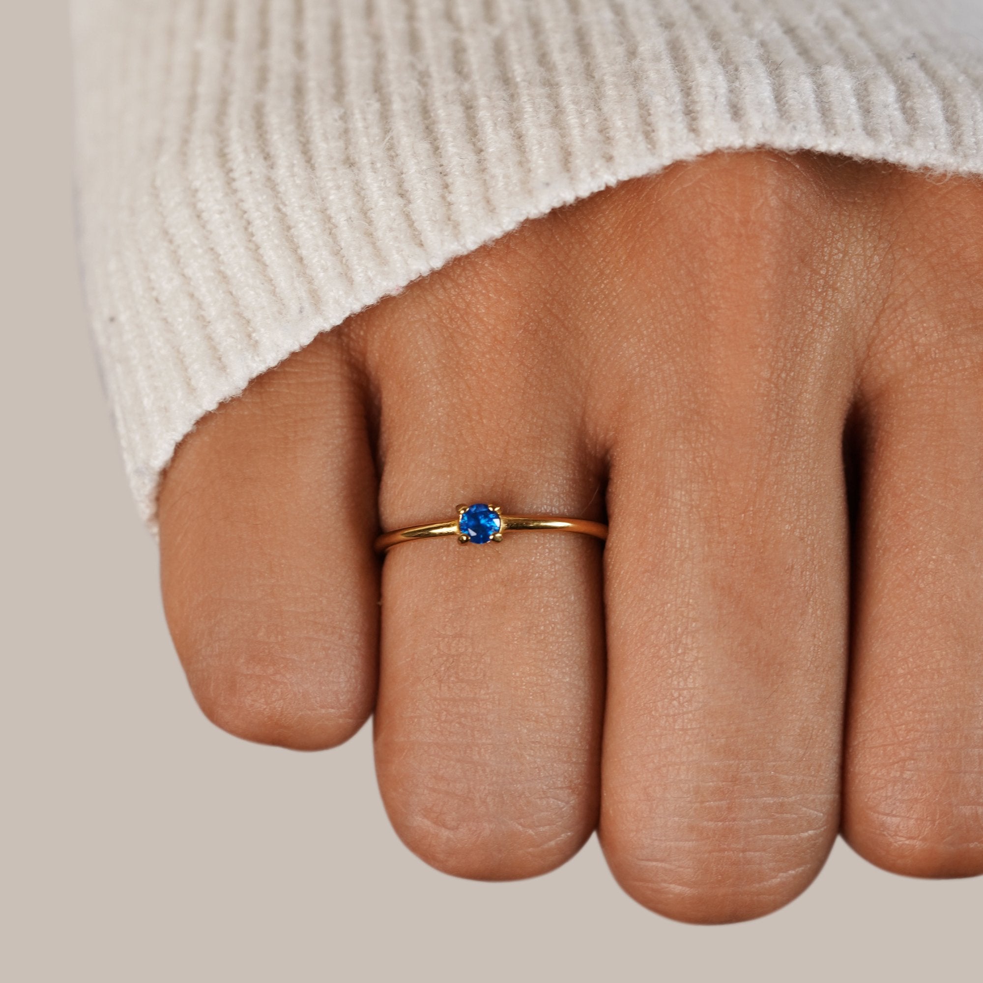 Birthstone 18K Gold Rings, worn on a finger with a cream knit sleeve, blue stone