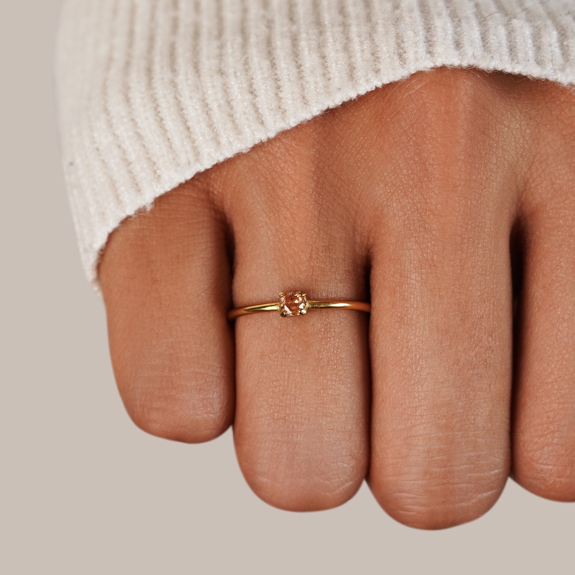 Birthstone 18K Gold Rings, worn on a hand with a cream knit sleeve, small peach stone