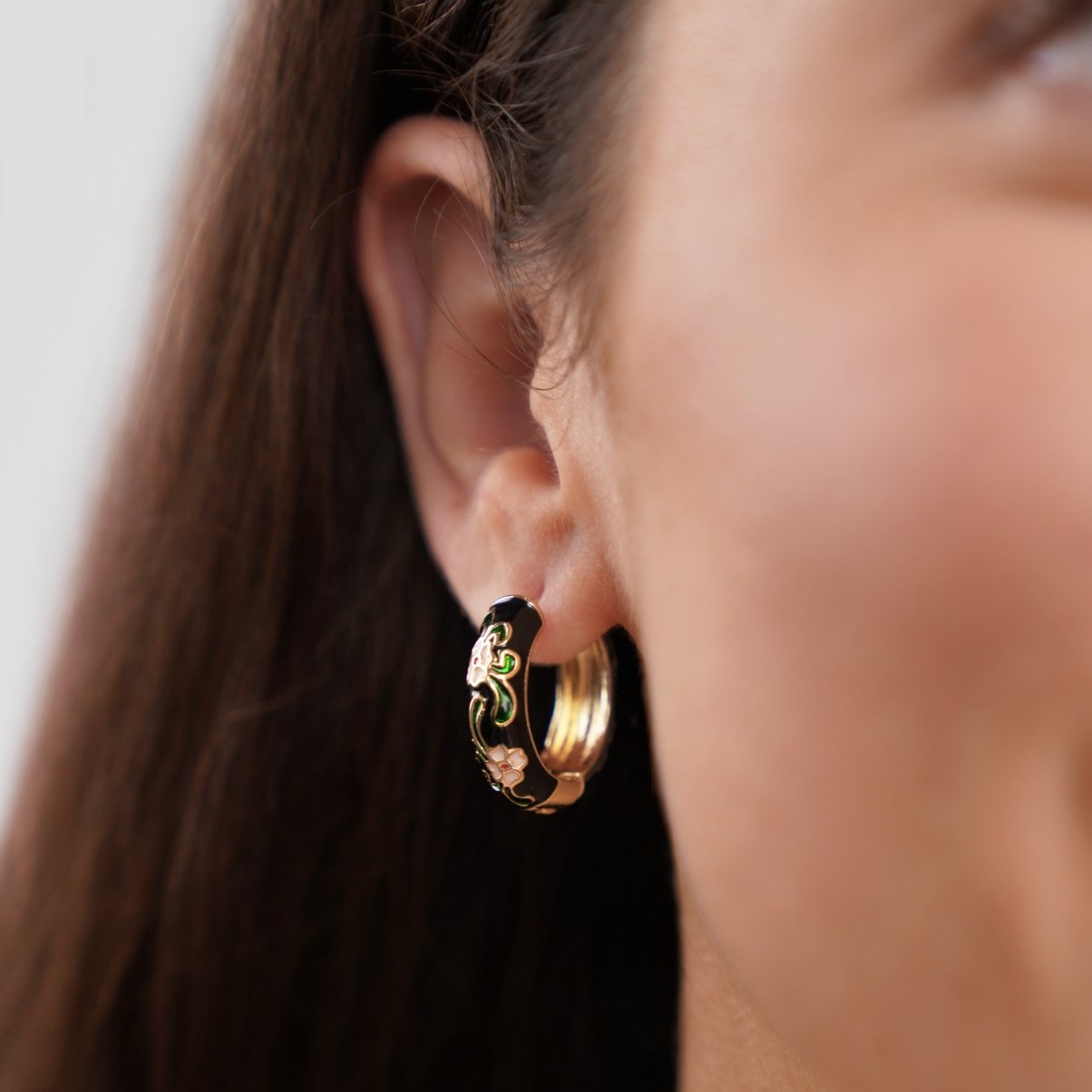 Black Gold Hoop Flower Earrings, worn on an ear, black enamel with green and pink floral detail