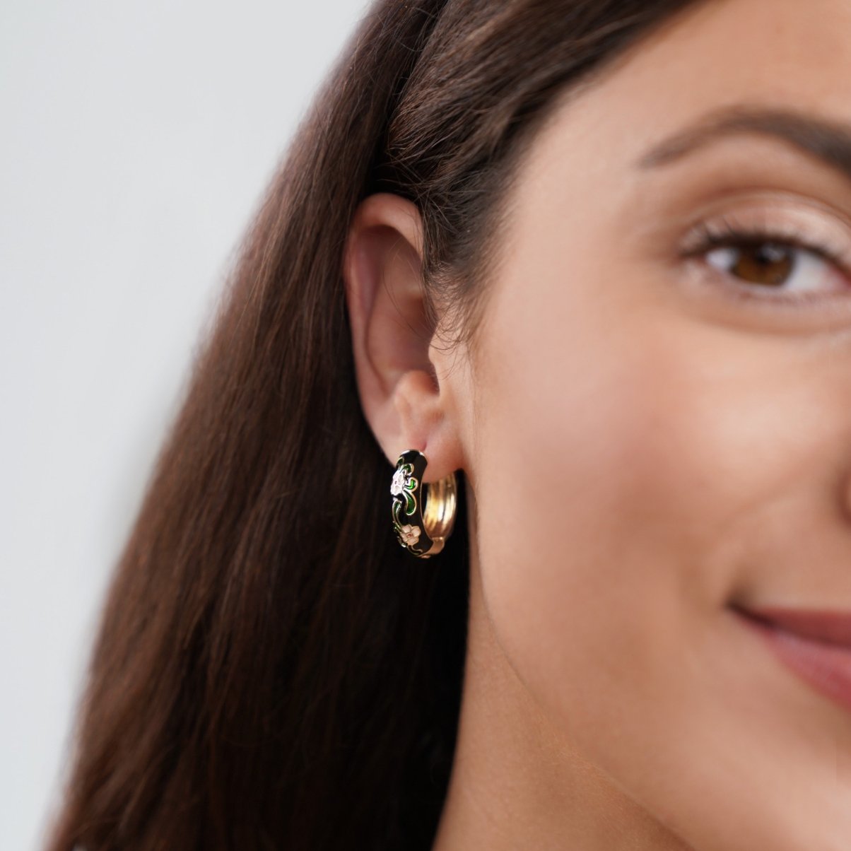 Black Gold Hoop Flower Earrings, worn in an ear, black enamel with green and white flowers