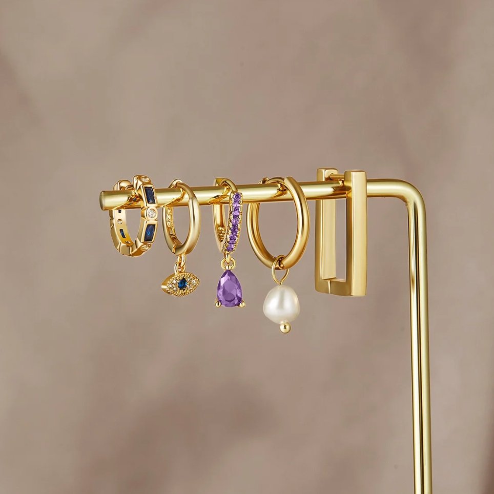 Blue Evil Eye Drop Earrings, several gold hoops on a display bar, with purple and pearl drops