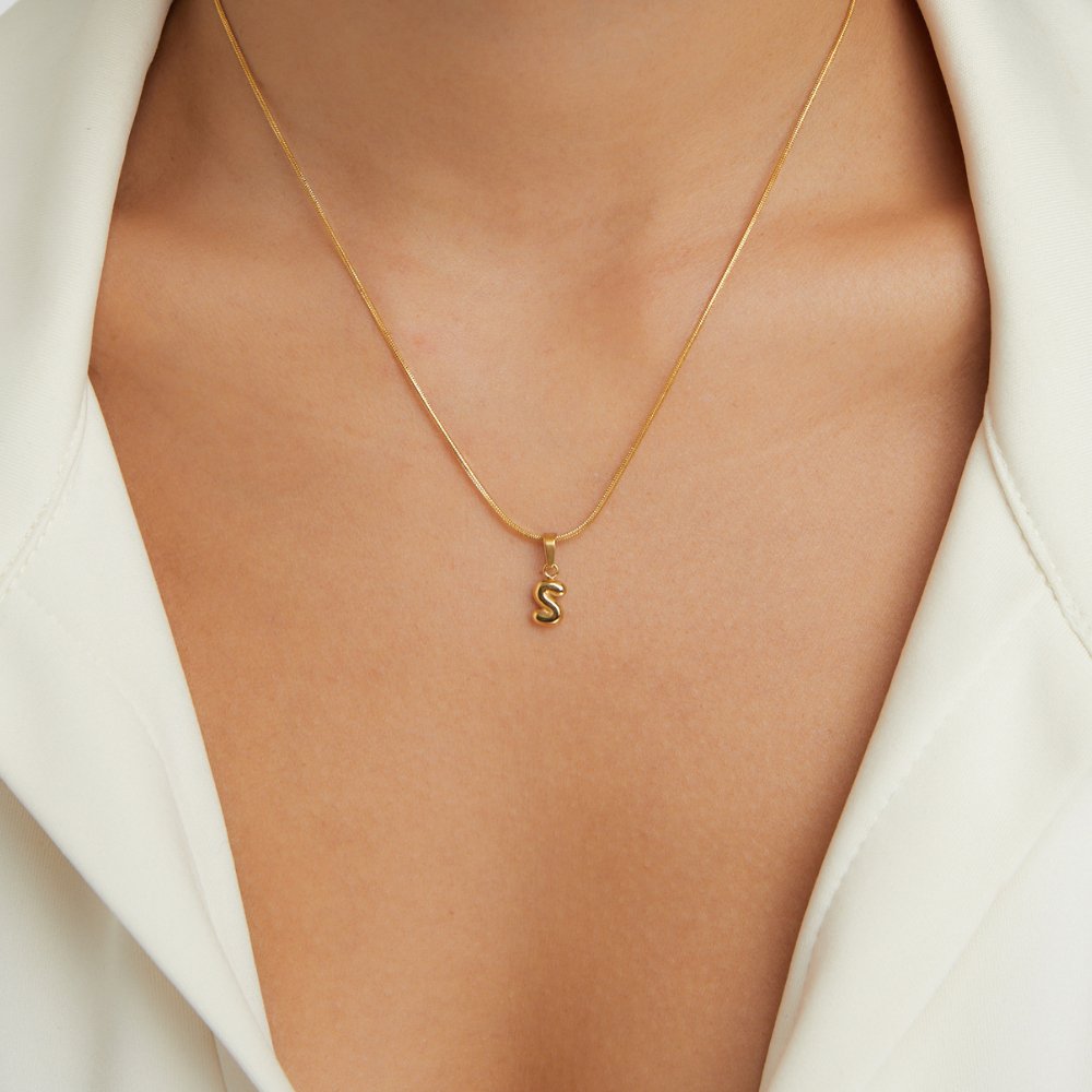 Bubble Letter Necklace, worn on a neck over a white collared top, puffy gold letter S pendant