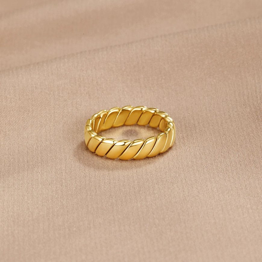 Calira Twisted Infinity Ring, gold ring with twisted ridges, lying on a beige fabric
