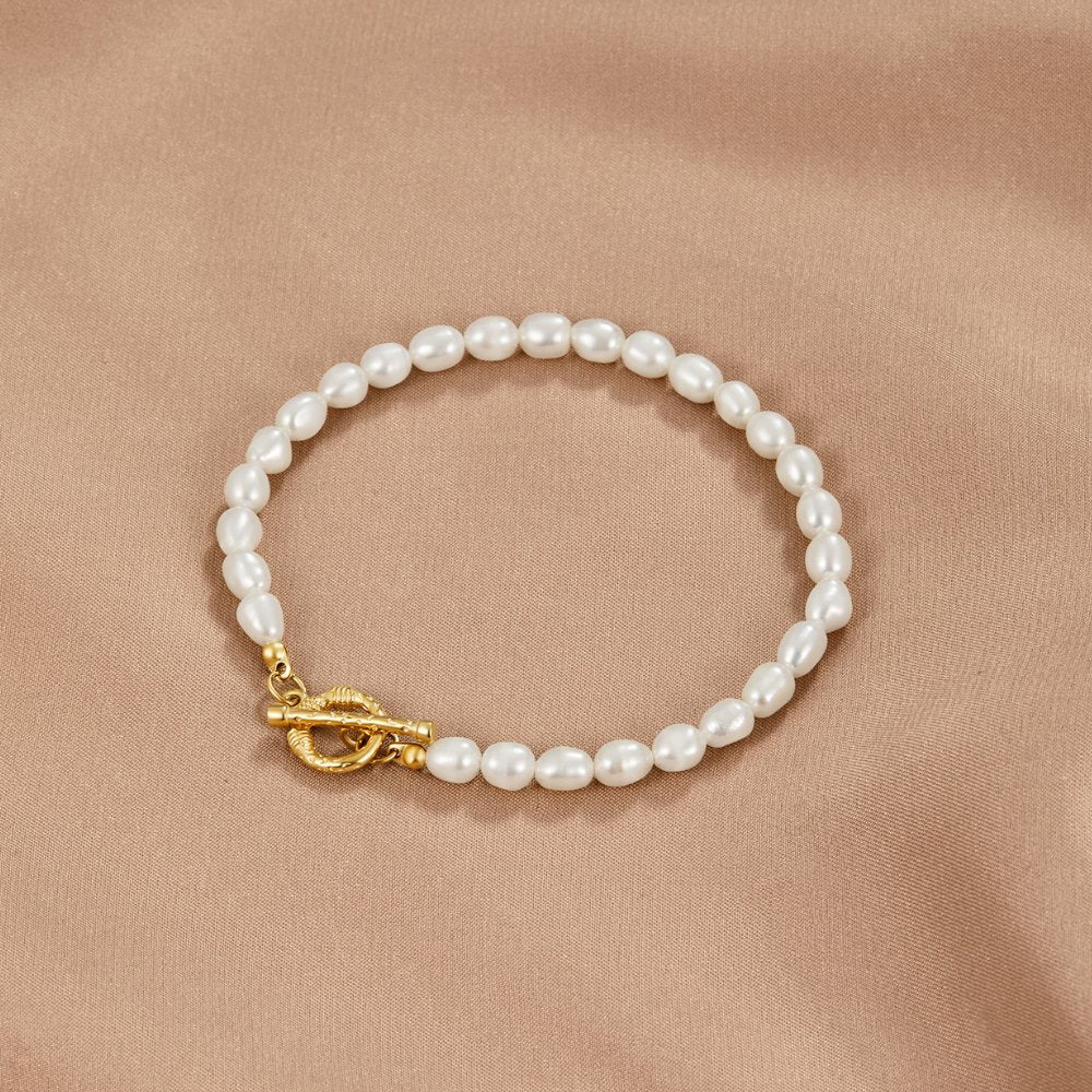 Cara Pearl Link Bracelet, laid flat on beige satin with white pearls and gold T-bar clasp