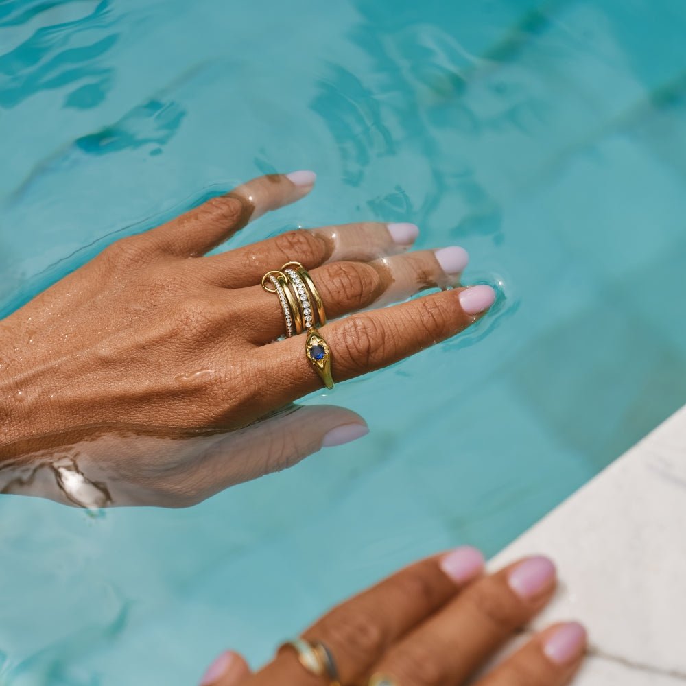Celestial Blue Star Ring, worn on a hand in pool water with stacked gold rings