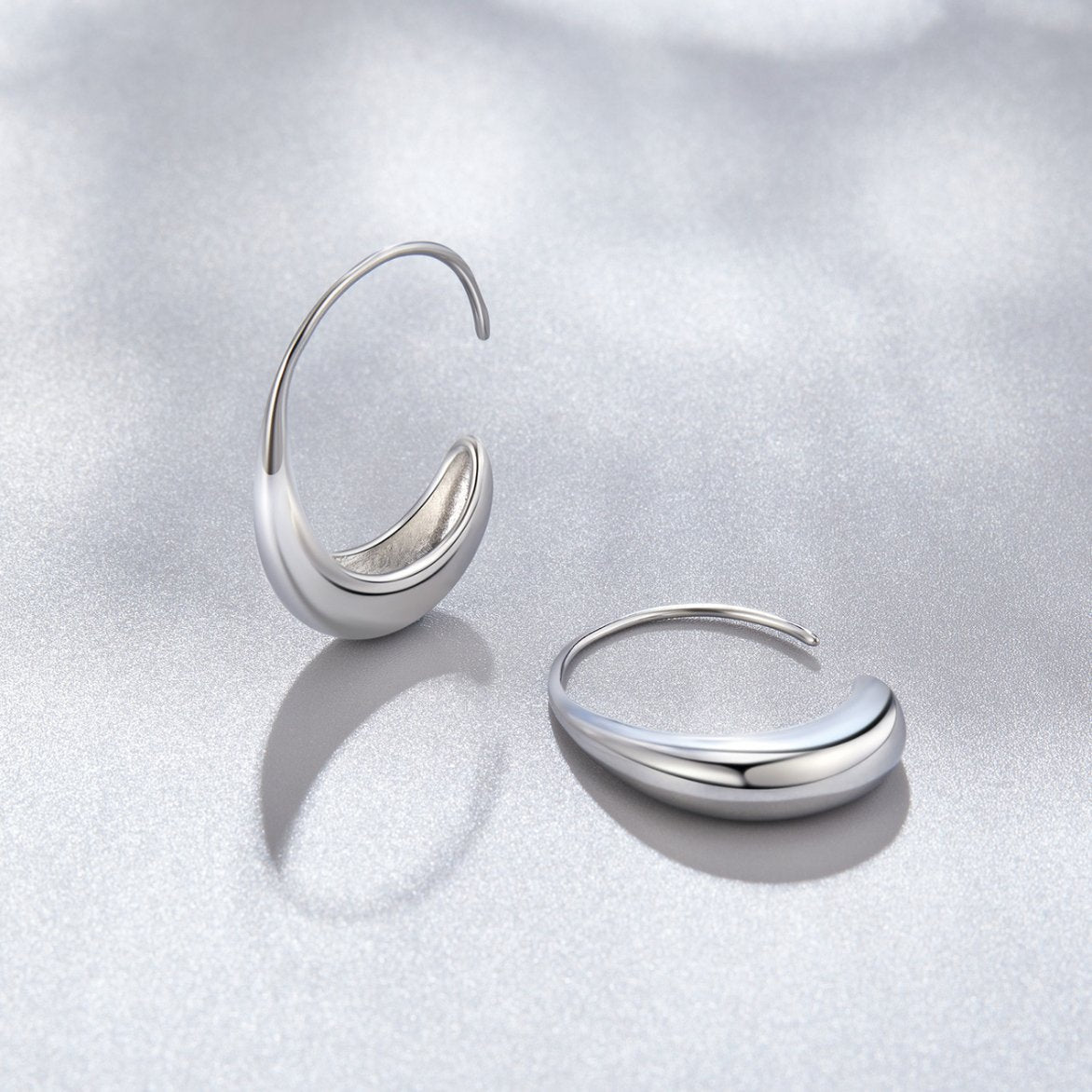 Classic Silver Drop Hoop Earrings, two polished silver hoop earrings lying on a pale grey surface